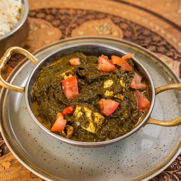 Far Eats Cafe's Palak Paneer, a vibrant green Indian spinach and cheese curry, garnished with fresh tomatoes.