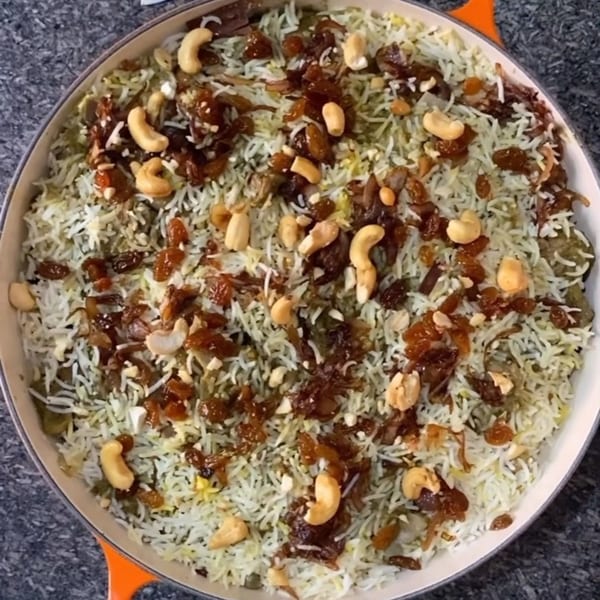 Overhead view of Indian biryani with rice, cashews, raisins, and fried onions in a white dish.
