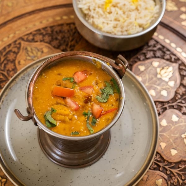 Indian dal in a copper pot with tomatoes and cilantro, alongside a bowl of rice.