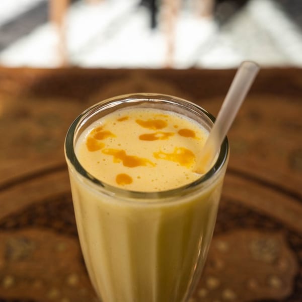 Close-up of a mango lassi with a straw, showing orange swirls on top.