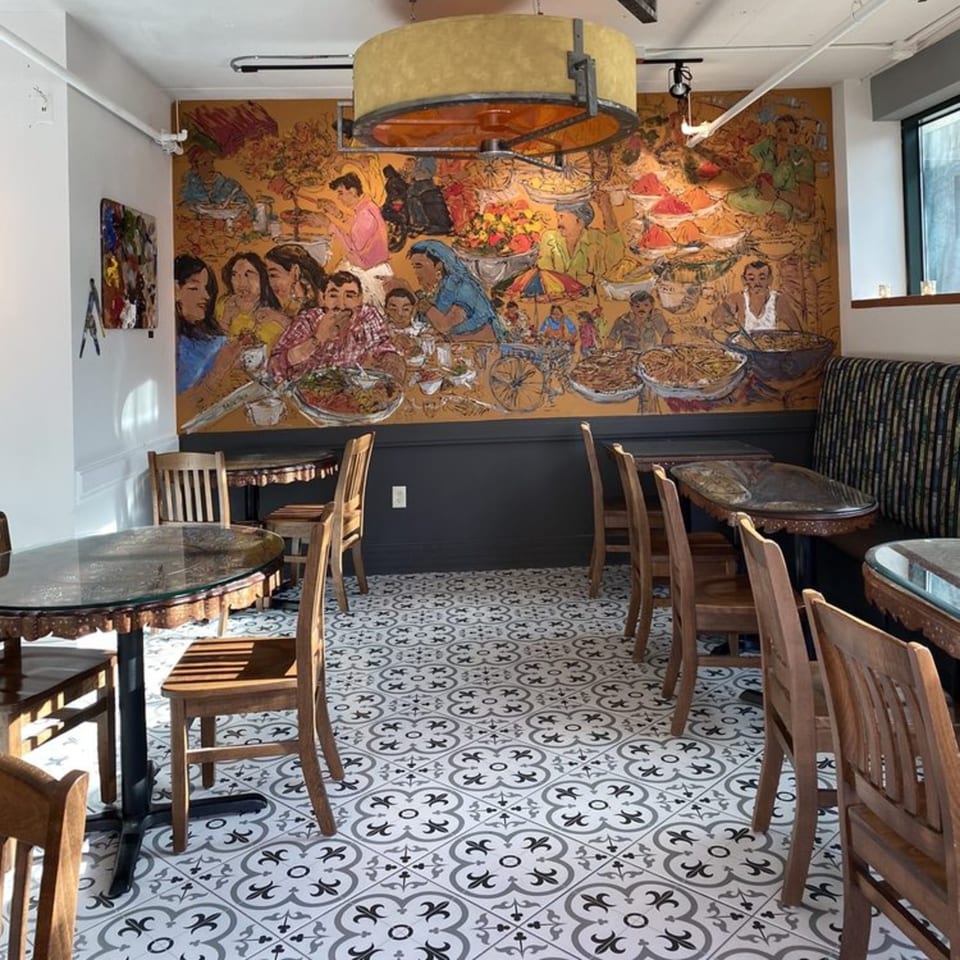 Far Eats Cafe dining room with a large Indian-themed mural, patterned floor, and wooden tables and chairs.