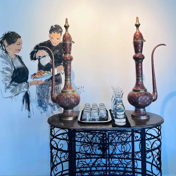 Indian-inspired mural of two chefs, with ornate brass pitchers and water glasses on a wrought iron table.