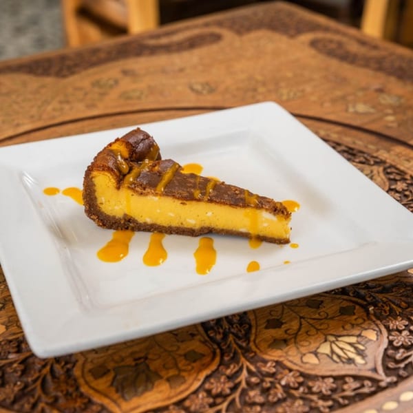 A slice of mango cheesecake with a chocolate crust and mango drizzle on a white plate.