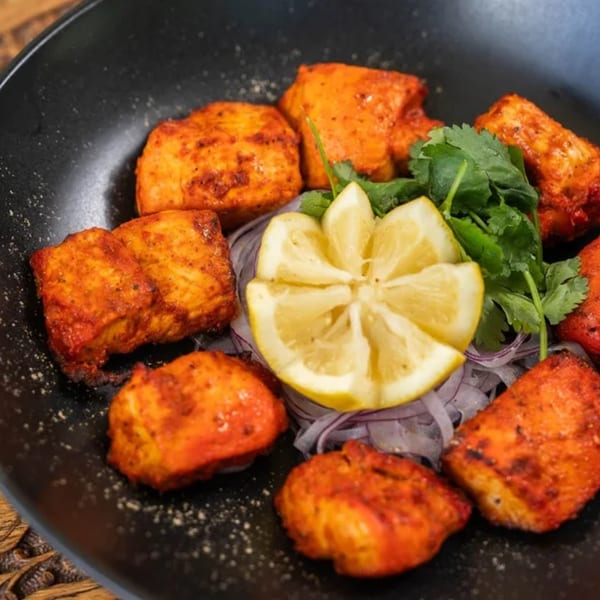 Indian paneer tikka, garnished with lemon, cilantro, and red onions, served in a black bowl.